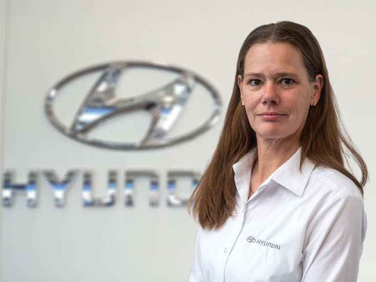 Auf dem Foto ist die Serviceassistentin Nicole Klockmann vor einer hellgrauen Wand mit dem Logo von Hyundai.